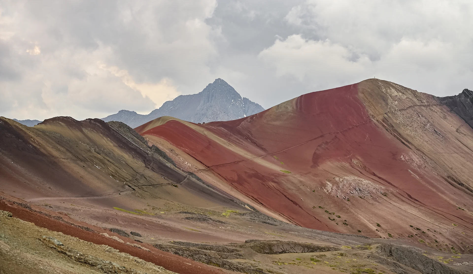 Rode en okerkleurige hellingen bij Vinicunca onder een bewolkte hemel.